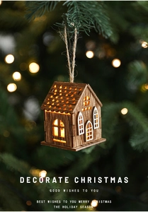Dettaglio casetta di Natale in legno a LED con luce calda appesa a un ramo d'albero