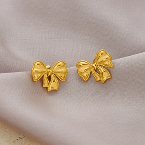 Elegant gold bow-shaped stainless steel earrings with matte texture on silk background