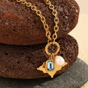 Macro shot of 18K gold plated necklace with pearl and blue gemstone on volcanic rock