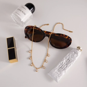 Detail of a golden water-drop pendant chain with tortoise sunglasses and luxury cosmetics