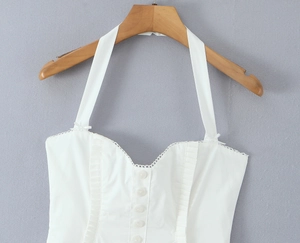 Detail eines weißen Neckholder-Kleids mit Knopfleiste und Lagen-Rüschendesign