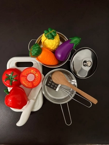 Flat lay of kids' kitchen set with stainless pots and toy vegetables on dark surface