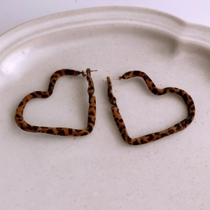 Macro shot of heart-shaped leopard print earrings with velvet flocking on a beige plate