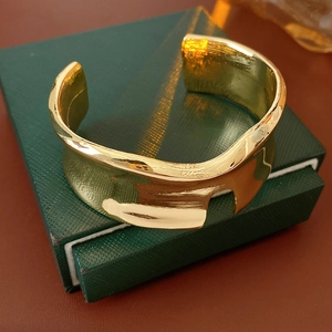 Dettaglio bracciale rigido dorato ondulato con intaglio ad H su confezione regalo verde