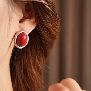 Close-up of a silver oval clip-on earring with a red gemstone on the ear