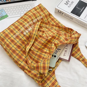 Close-up of yellow and orange plaid canvas tote bag with ZAKKA embroidery on a desk