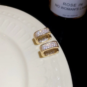 Macro shot of gold square hoop earrings with crystal pavé on white ceramic dish