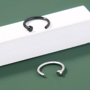 Detail of silver and black U-shaped stainless steel nose rings on a white cube display