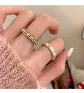 Close-up of stacked gold pearl rings and cream enamel flower ring on a hand