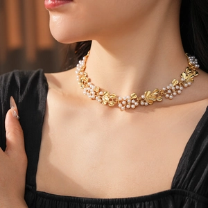 Detail of vintage gold leaf choker necklace with pearls worn by model in warm lighting