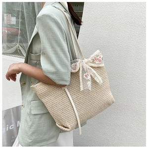 Detail of straw tote bag featuring white lace bow and rose embroidery accents