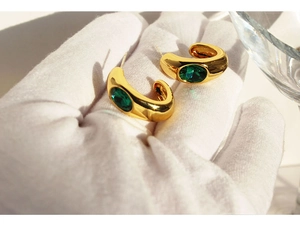 Macro detail of gold C-shaped earrings with emerald zircon held in a gloved hand