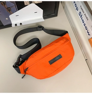 Detail of orange nylon chest bag with rubber brand logo and black buckle strap