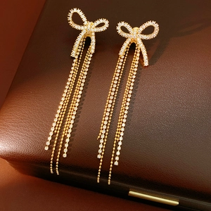 Detail view of 18k gold bow earrings with crystal tassels on premium brown leather