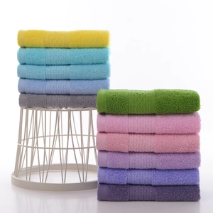 Soft cotton hand towels in various pastel colors with textured woven borders on a white rack
