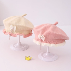 Detailed close-up of knitted baby beret featuring lace bow and scalloped edge detail