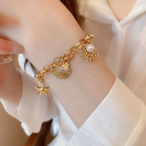 Detail of a gold ocean charm bracelet with starfish, seashell and pearl on a wrist