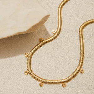 Klassische 18K vergoldete Schlangenkette mit weißen Zirkonia-Anhängern auf beigem Hintergrund