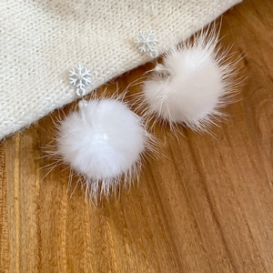Dettaglio degli orecchini a fiocco di neve con pompon bianco su tessuto a maglia morbido