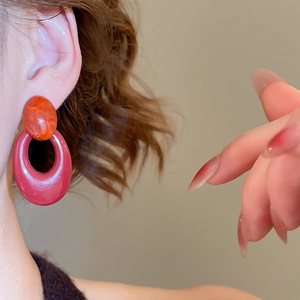 Macro shot of retro oval acrylic pendant earrings in red and amber tones on model