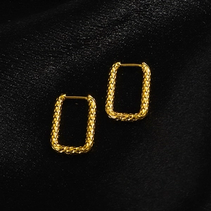 Close-up of golden rectangular hoop earrings with hammered texture on black silk fabric