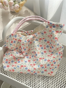 Detail of floral canvas tote bag featuring pink woven rope handles and a brand label