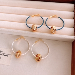 Detailed view of blue and white 18K gold plated knot hoop earrings on a beige tray