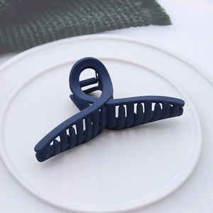 Close-up of deep blue matte hair claw clip with twisted cross design on a white plate