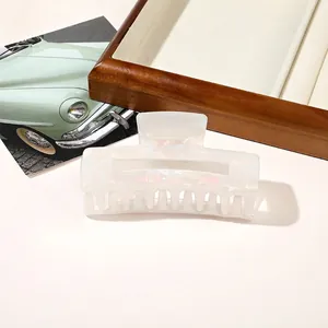 Detail of pearlescent white rectangular claw clip with iridescent finish on a white surface