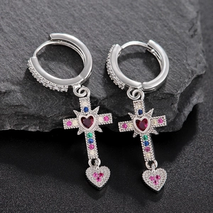 Silver cross earrings with red heart stones and zircon accents on a dark stone surface