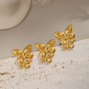 Three gold butterfly rings displayed on textured beige stone with a reflective mirror