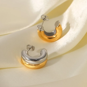 Detailansicht der zweifarbigen C-förmigen Ohrringe in Gold und Silber auf Seidenstoff