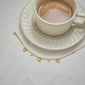 Golden heart charm bracelet on a textured cloth next to a coffee cup in a lifestyle setting