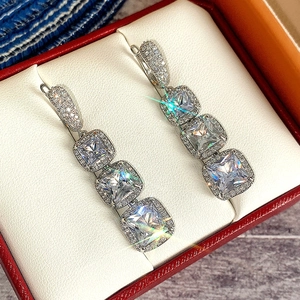 Detailed close-up of square zircon drop earrings with pavé halo setting in a red jewelry box