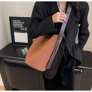 Detailed view of brown suede bucket bag with wide adjustable shoulder strap on a model