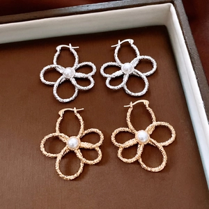 Detailed view of hollow flower earrings with central pearls in gold and silver finishes