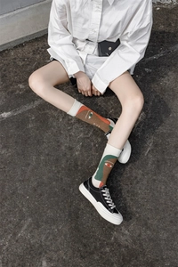 Close-up of crew socks with colorful abstract face design worn by a model in nature