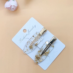 Detail of two resin hair clips with gold foil flakes and light gold metal duckbill clips