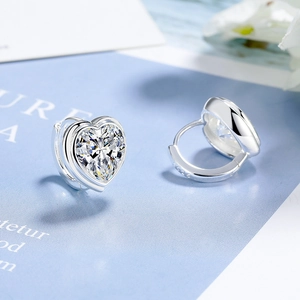 Detailed macro shot of silver huggie earrings featuring sparkling heart-shaped zirconia stones