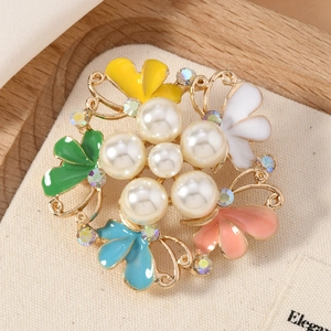 Close-up of golden floral brooch with colorful enamel petals and faux pearl center
