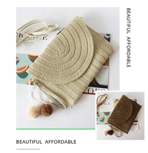 Close-up of straw woven envelope clutch bag with pompom charms and wristlet strap