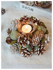 Close-up of pinecone candle holder with forest greenery and snow effect on a white surface