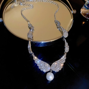 Close-up of silver angel wing necklace with zircon stones and a pearl on a black surface