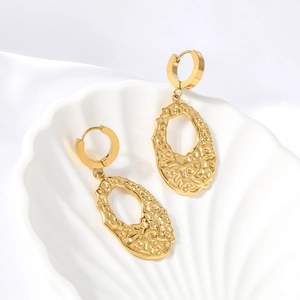 Elegant irregular textured gold hoop earrings displayed on white silk and shell background