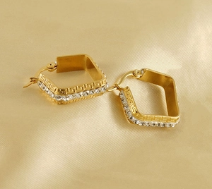 Macro detail of gold earrings with square zircon settings and greek key patterns