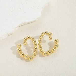 Detail of gold beaded C-shaped hoop earrings on a textured off-white background