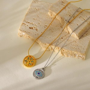 Detail of gold tree of life and silver evil eye pendants on stone with leaf shadows