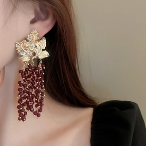 Close-up of golden leaf earrings with red grape-shaped bead tassels worn by a model