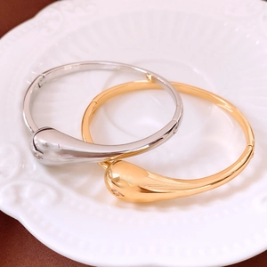 Close-up of gold and silver water-drop bracelets on a white ceramic tray with polished finish