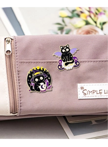 Detail of fantasy black cat enamel pins with wizard hat and skull on a purple bag